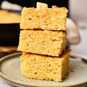 Three stacked slices of air fryer cornbread on a plate, with a pat of butter melting on top.