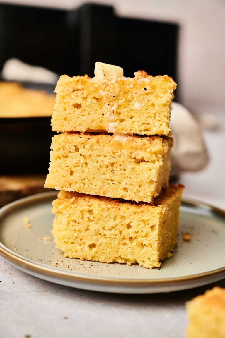 Three stacked slices of air fryer cornbread on a plate, with a pat of butter melting on top.