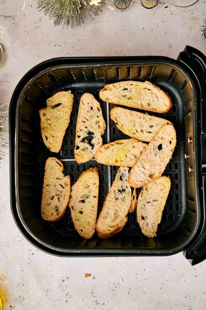 Slices of bread with herbs placed inside an air fryer basket.