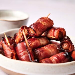 A plate of bacon-wrapped dates secured with toothpicks, stacked high.