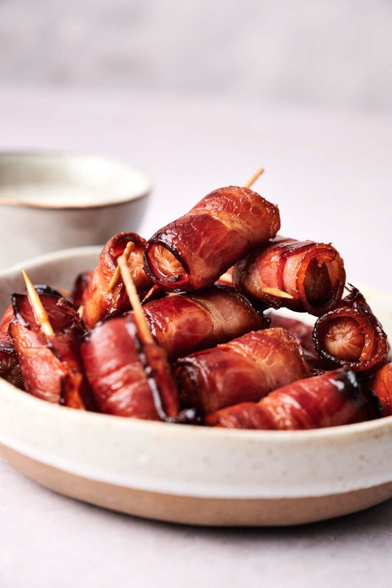 A plate of bacon-wrapped dates secured with toothpicks, stacked high.