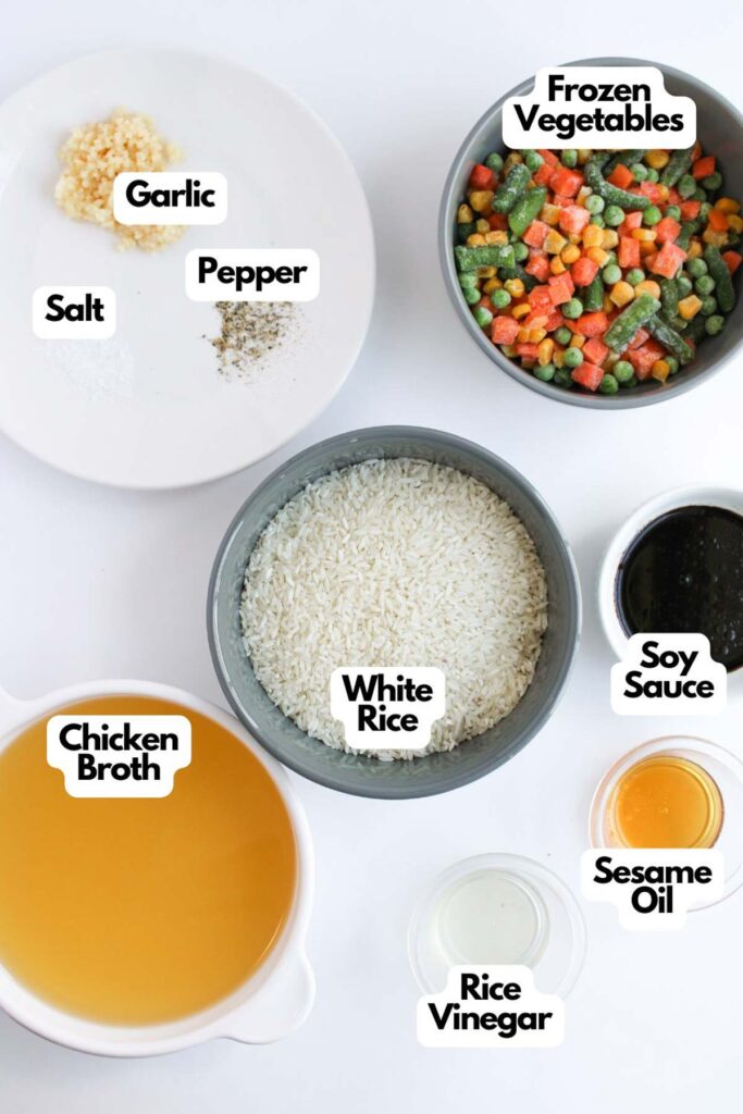 Ingredients displayed on a table include garlic, frozen vegetables, and white rice ready for an Oven Baked Fried Rice dish. Soy sauce, chicken broth, sesame oil, rice vinegar, salt, and pepper complete the flavorful ensemble.