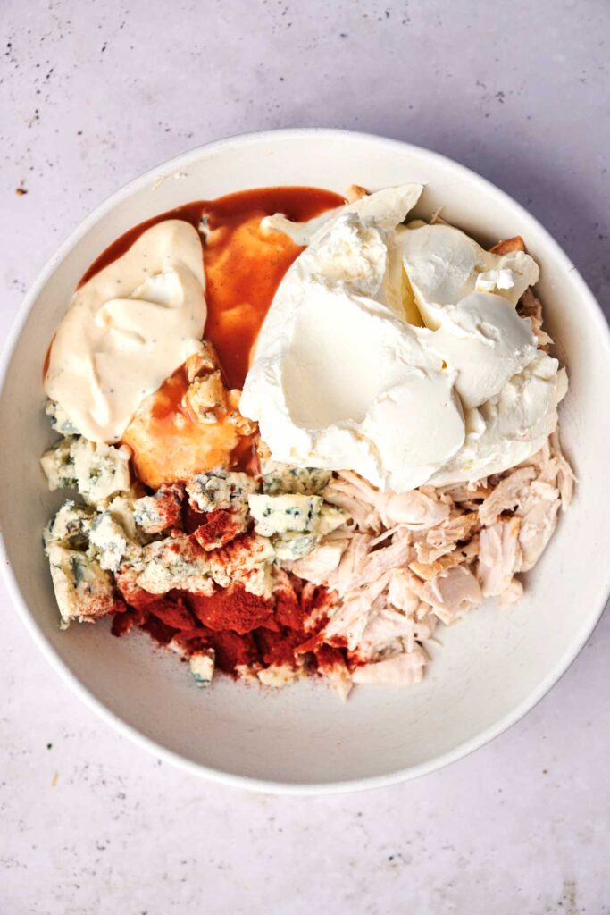 A bowl with chicken, blue cheese, cream cheese, mayonnaise, hot sauce, and paprika.