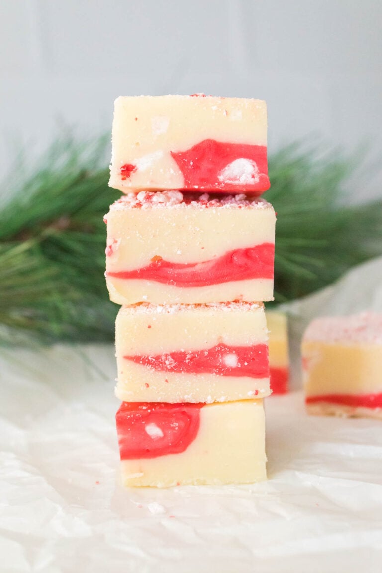 A stack of candy cane fudge swirled with red and white sits on parchment paper, framed by pine branches in the background.