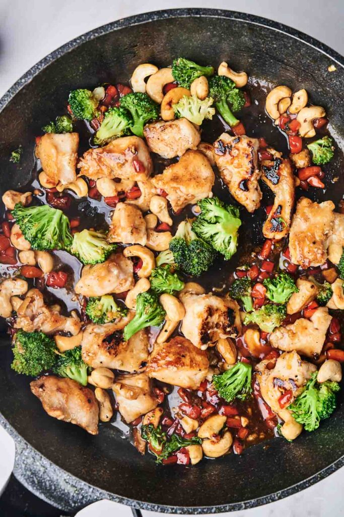 Cashew Chicken stir-fried with broccoli and bell peppers in a sizzling pan.