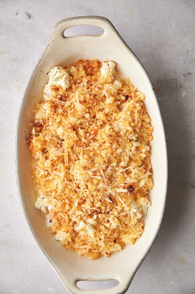 A baking dish containing cauliflower gratin topped with breadcrumbs and cheese on a gray countertop.