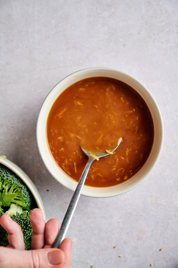 A bowl of brown soup with a spoon, next to a bowl containing broccoli florets.