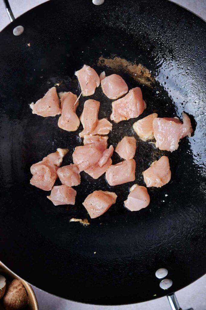 Raw diced chicken pieces in a large black pan.
