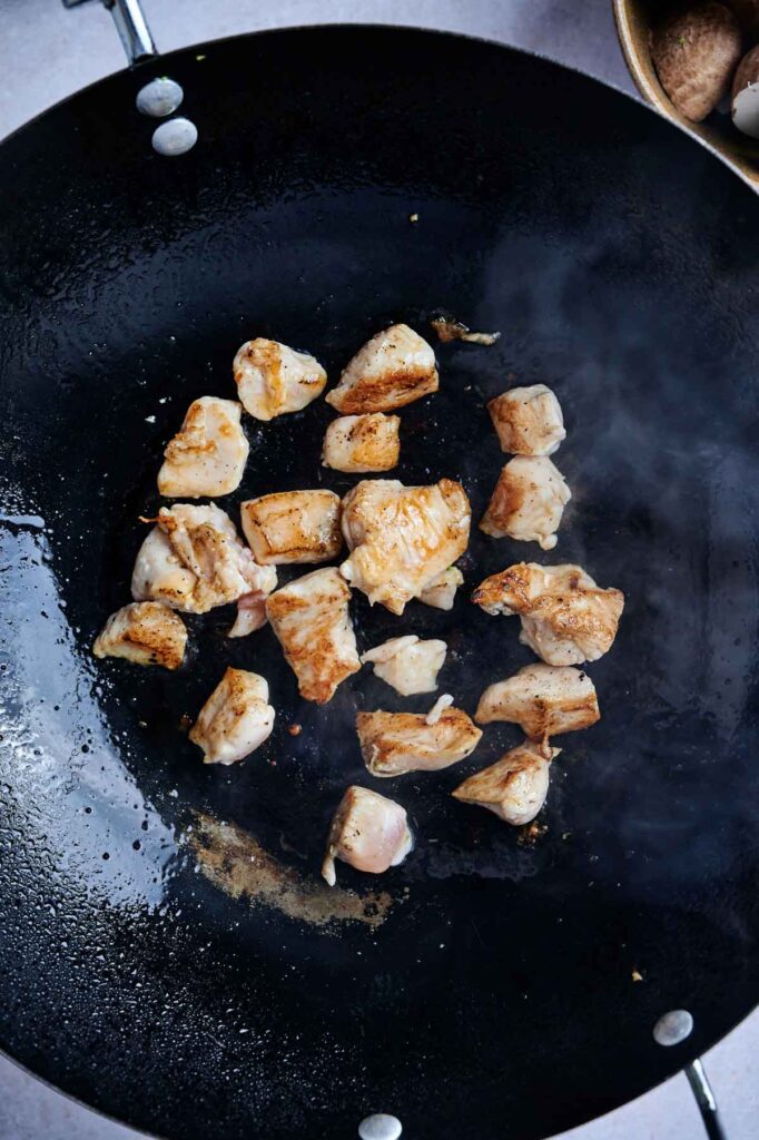 Chunks of chicken cooking in a black wok with visible steam rising.