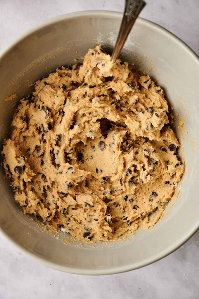 A mixing bowl filled with chocolate chip cookie dough and a spoon.