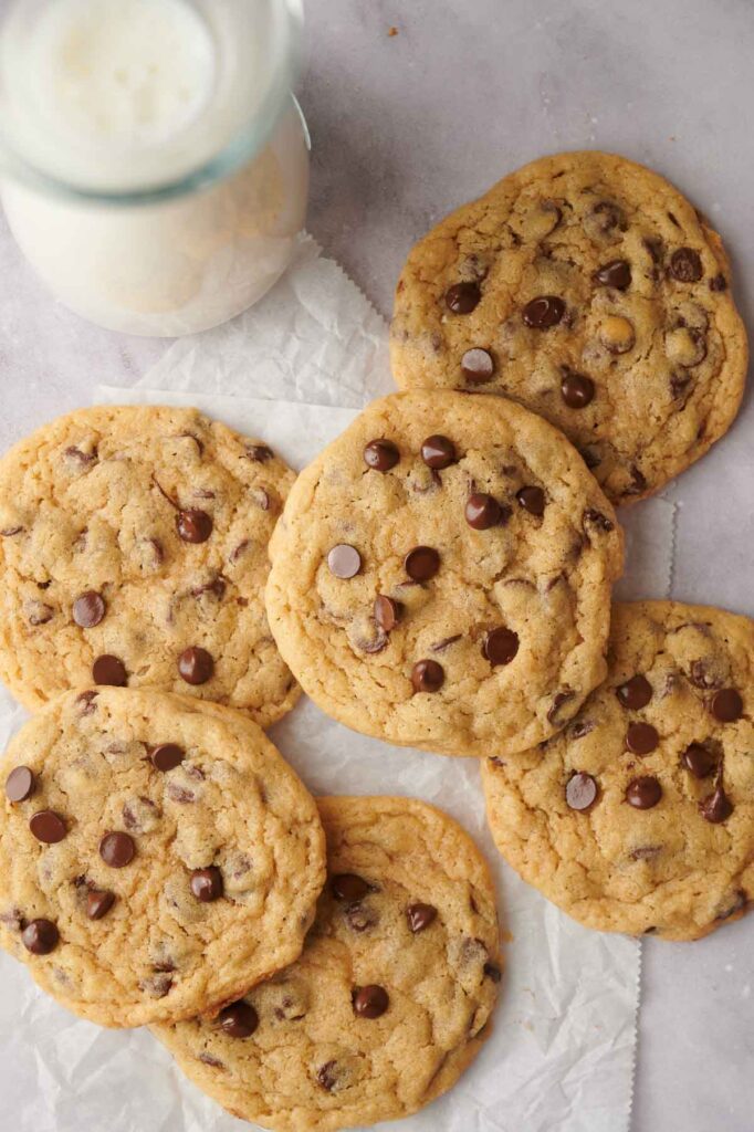 Chocolate chip cookies on parchment paper with a glass of milk nearby.
