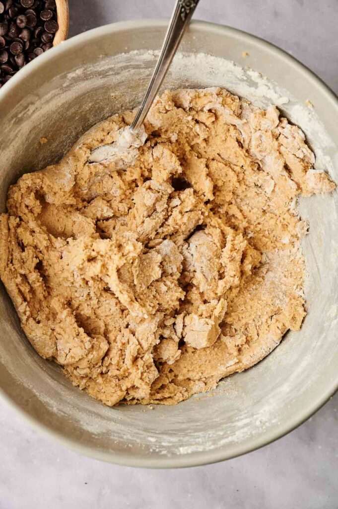 A large bowl filled with cookie dough and a spoon on a marble surface.
