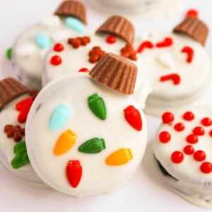 Oreo Christmas Ornament Cookies are decorated with white icing, red and green candies, and mini peanut butter cups on top, transforming the classic treat into festive holiday delights.