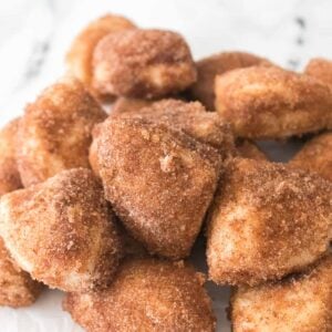 A tempting pile of Cinnamon Sugar Biscuit Bites rests on a pristine white surface, each piece perfectly coated in a sweet, spiced bliss.