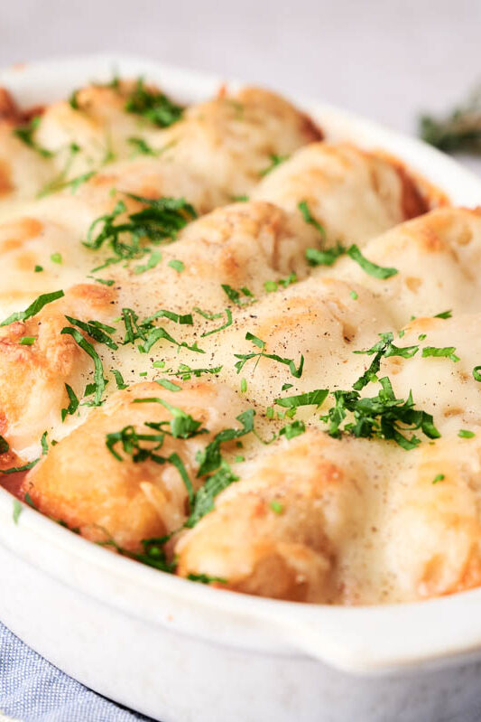 A baked dish of stuffed shells topped with melted cheese and garnished with chopped herbs in a white oval dish.