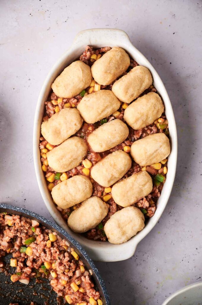 Oval dish with a layer of tater tots on ground meat mixture with corn and peas.