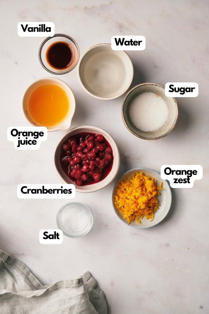 Ingredients on a surface: bowls of vanilla, water, sugar, orange juice, cranberries, orange zest, and salt.