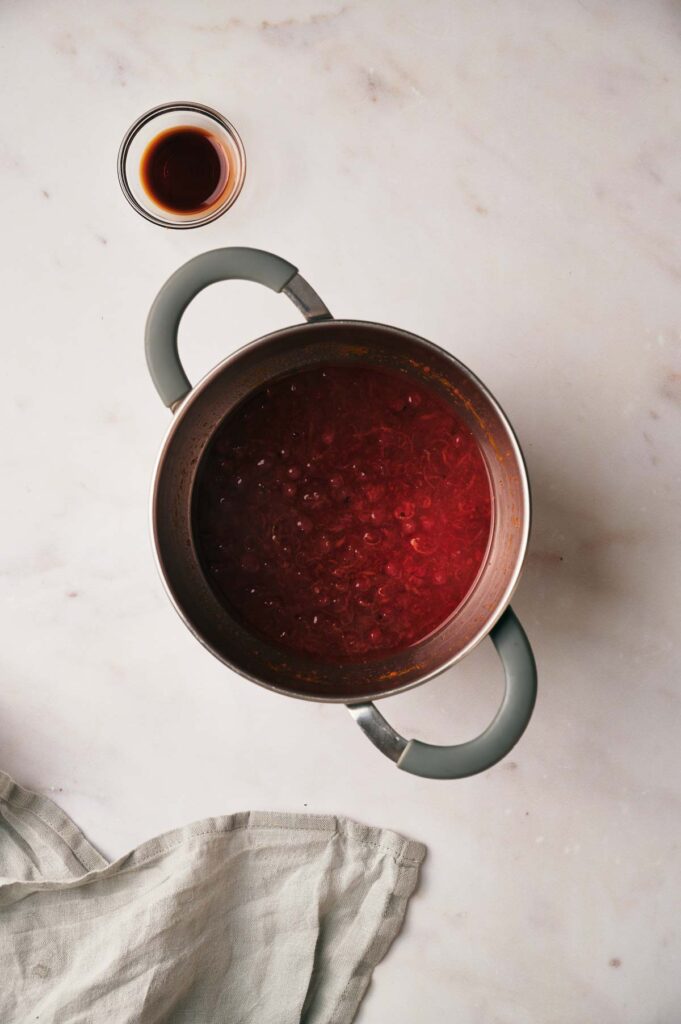A pot of red sauce on a marble surface with a small cup of soy sauce beside it and a cloth nearby.