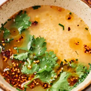 A steaming bowl of delicious egg drop soup, delicately garnished with fresh cilantro, chives, and a sprinkle of red chili flakes.