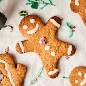 Air fryer gingerbread cookies decorated with icing and a small candy heart, surrounded by other cookies and festive decorations on parchment paper.