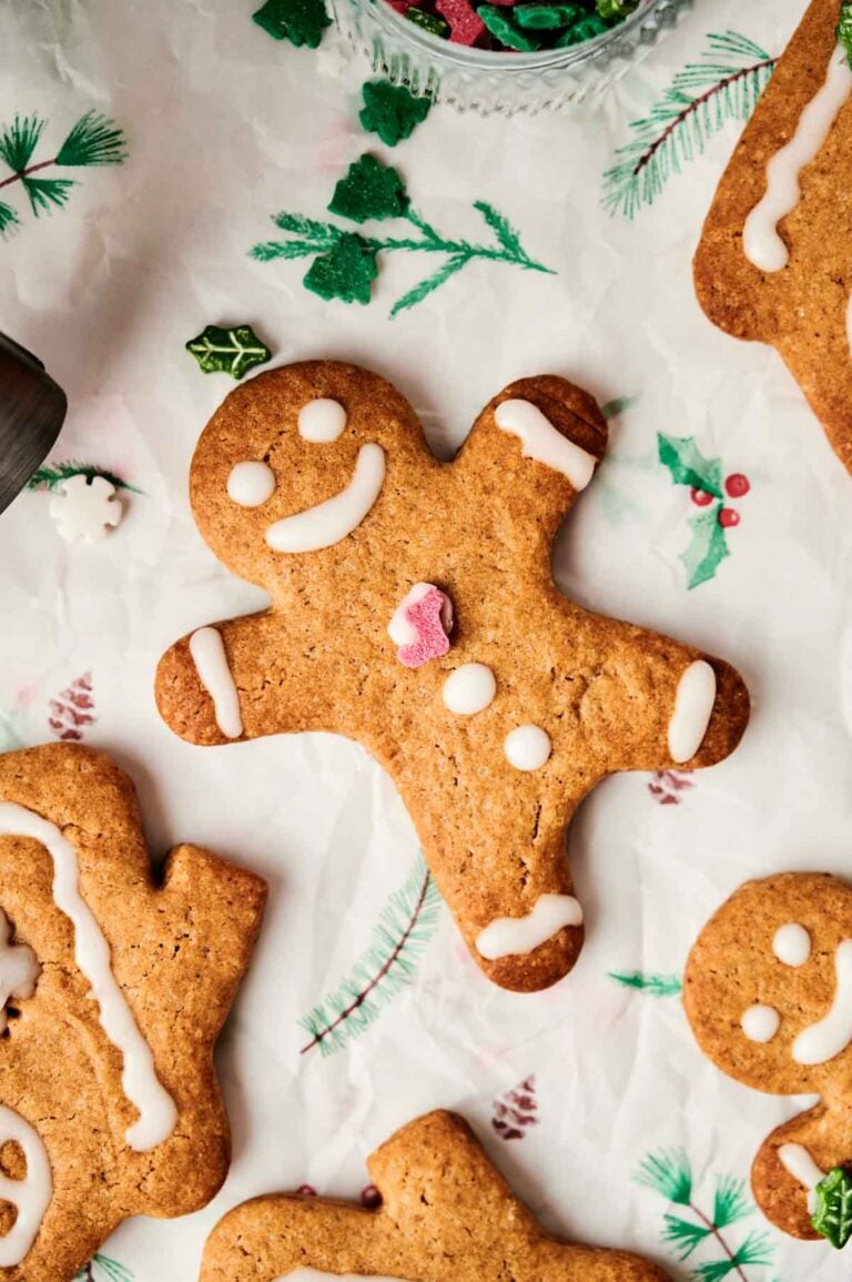 Air fryer gingerbread cookies decorated with icing and a small candy heart, surrounded by other cookies and festive decorations on parchment paper.