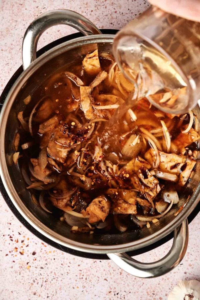 Adding broth to a pot with mushrooms, onions, and spices creates a comforting base reminiscent of a hearty kimchi stew.