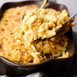 A serving of baked macaroni and cheese is being scooped from a dish with a spoon. The casserole is topped with a golden, crispy crust.