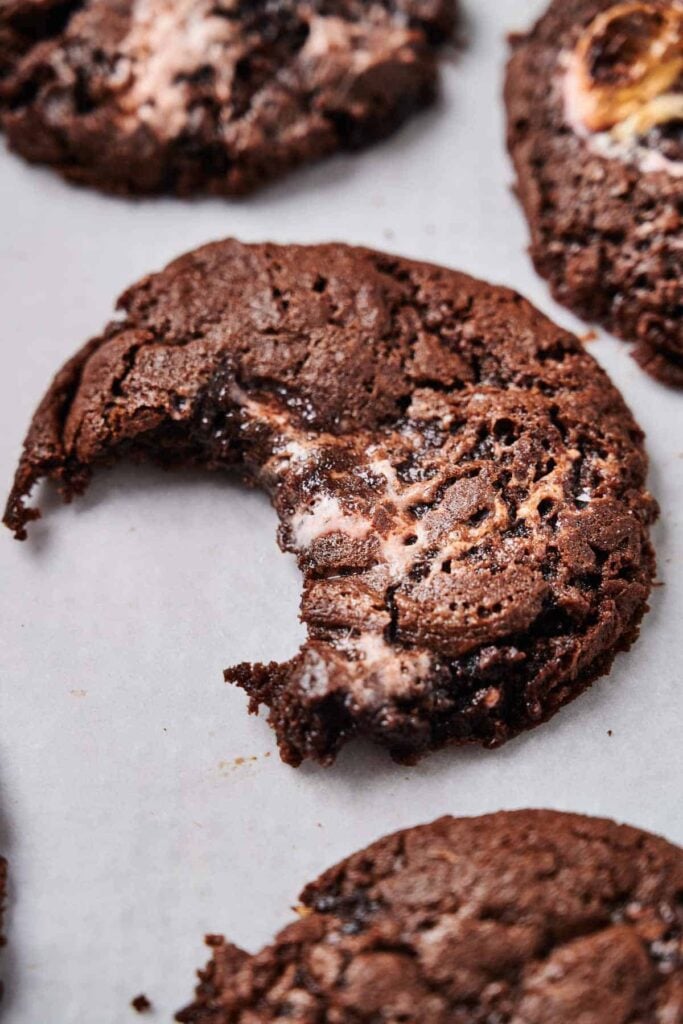 Close-up of chocolate cookies with melted marshmallow filling on a baking sheet, one with a bite taken out.