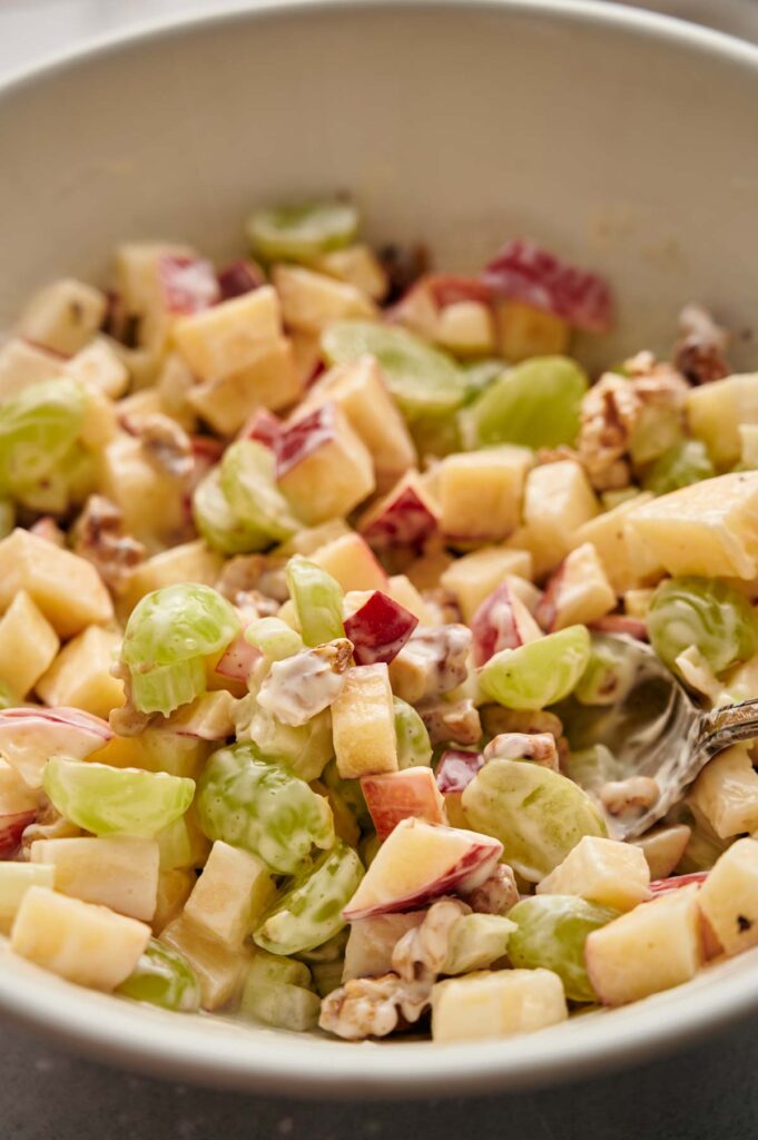 A bowl of fruit salad with chopped apples, grapes, and walnuts, mixed with a creamy dressing.
