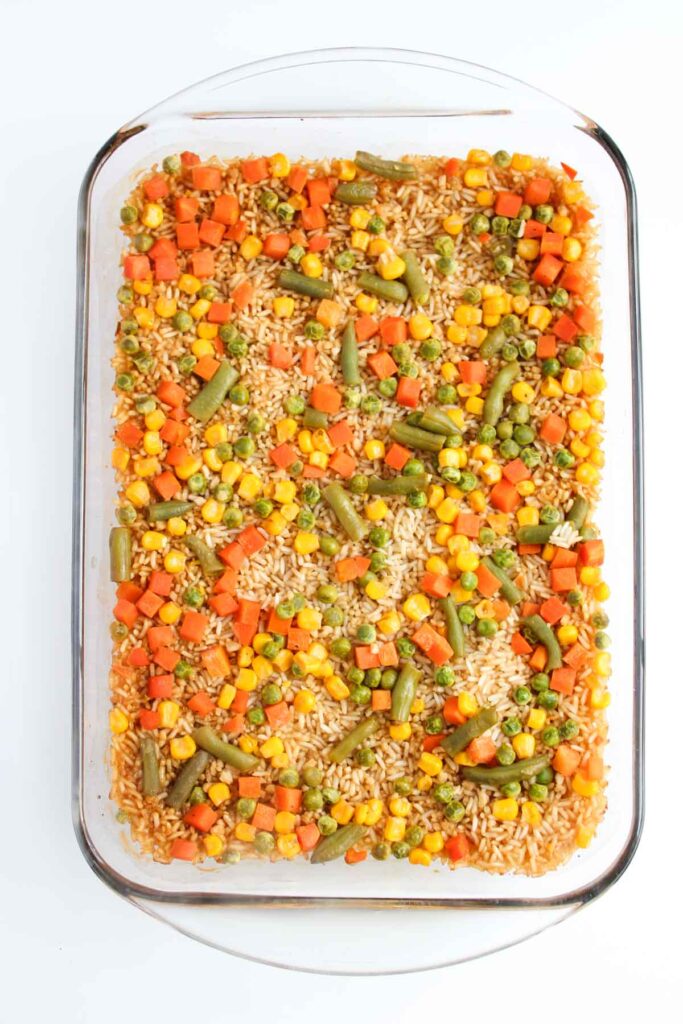 A glass baking dish brimming with colorful oven-baked fried rice, featuring a vibrant mix of peas, corn, carrots, and green beans.
