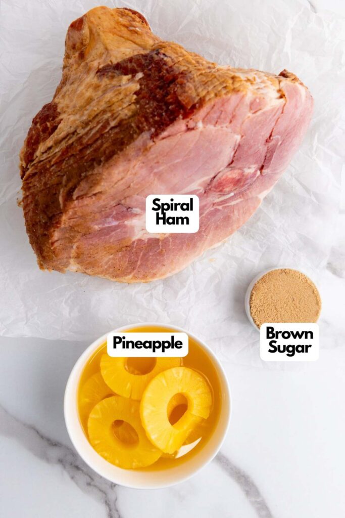 Spiral ham on paper with labeled ingredients: brown sugar and pineapple slices in a bowl, set against a marble surface.