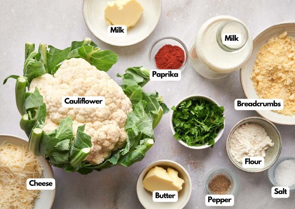 A cauliflower sits on a counter surrounded by labeled bowls of cheese, milk, paprika, breadcrumbs, flour, parsley, butter, pepper, and salt&mdash;perfect ingredients for a vegetarian twist on chicken noodle casserole.