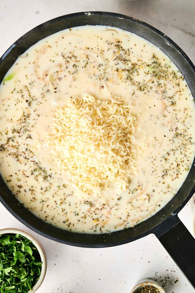 A skillet filled with creamy sauce, chunks of chicken noodle casserole, sprinkled with herbs and topped with shredded cheese.