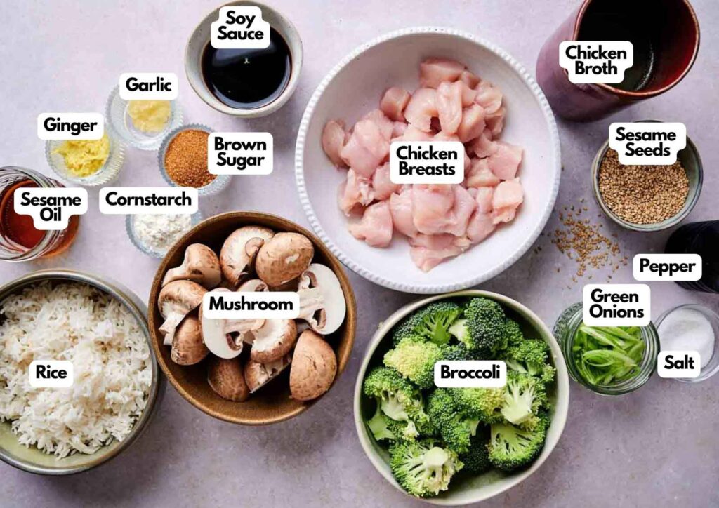 Ingredients for chicken and broccoli stir fry laid out on a white surface, including chicken breasts, broccoli, mushrooms, soy sauce, garlic, ginger, cornstarch, sesame oil, brown sugar, chicken broth, sesame seeds, green onions, rice, salt, and pepper.