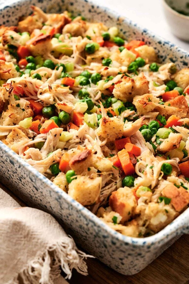 A casserole dish filled with a delicious chicken and stuffing casserole, featuring chunks of bread, shredded chicken, peas, carrots, and herbs.