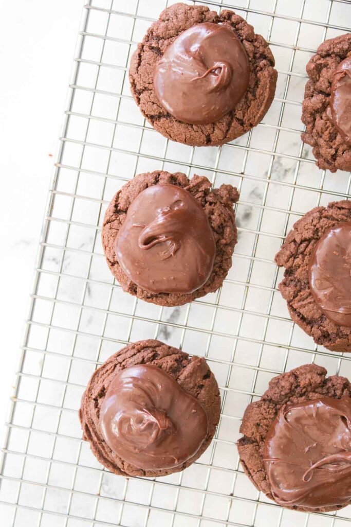 Chocolate cherry cookies topped with glossy chocolate icing rest enticingly on a cooling rack.