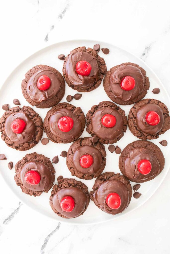 A plate of chocolate cherry cookies topped with luscious chocolate frosting and juicy cherries.