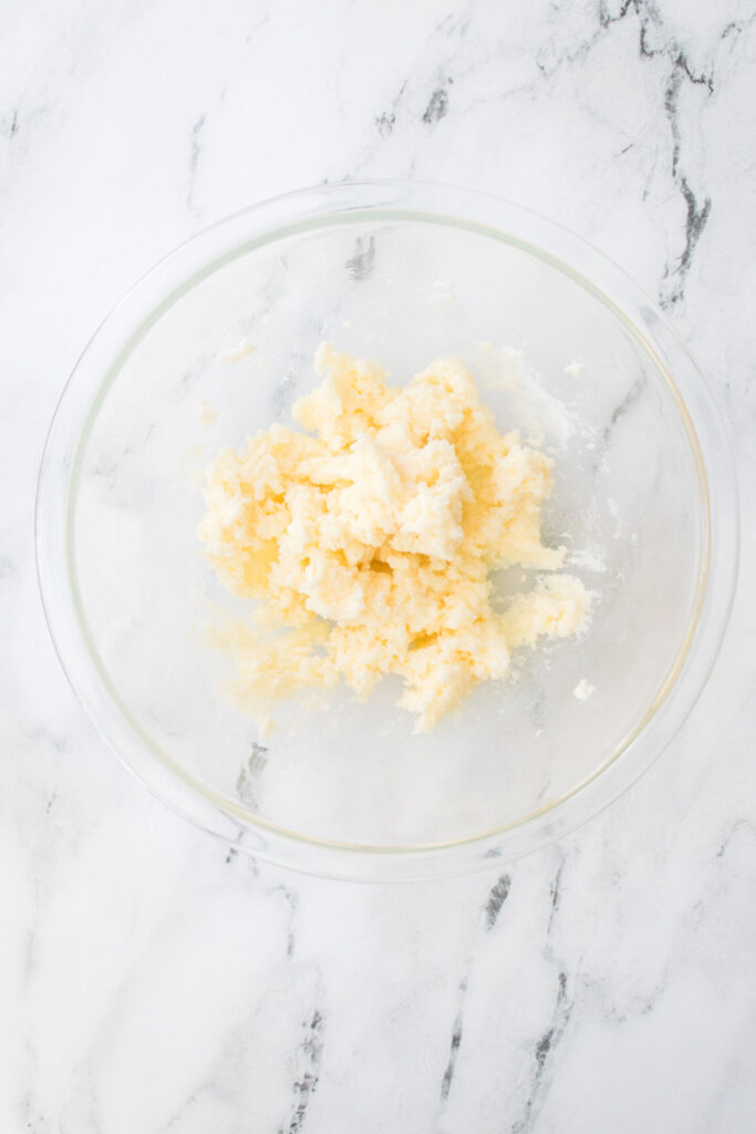 On a marble countertop, a glass bowl holds a mixture of creamed butter and sugar, the perfect base for crafting delectable chocolate cherry cookies.