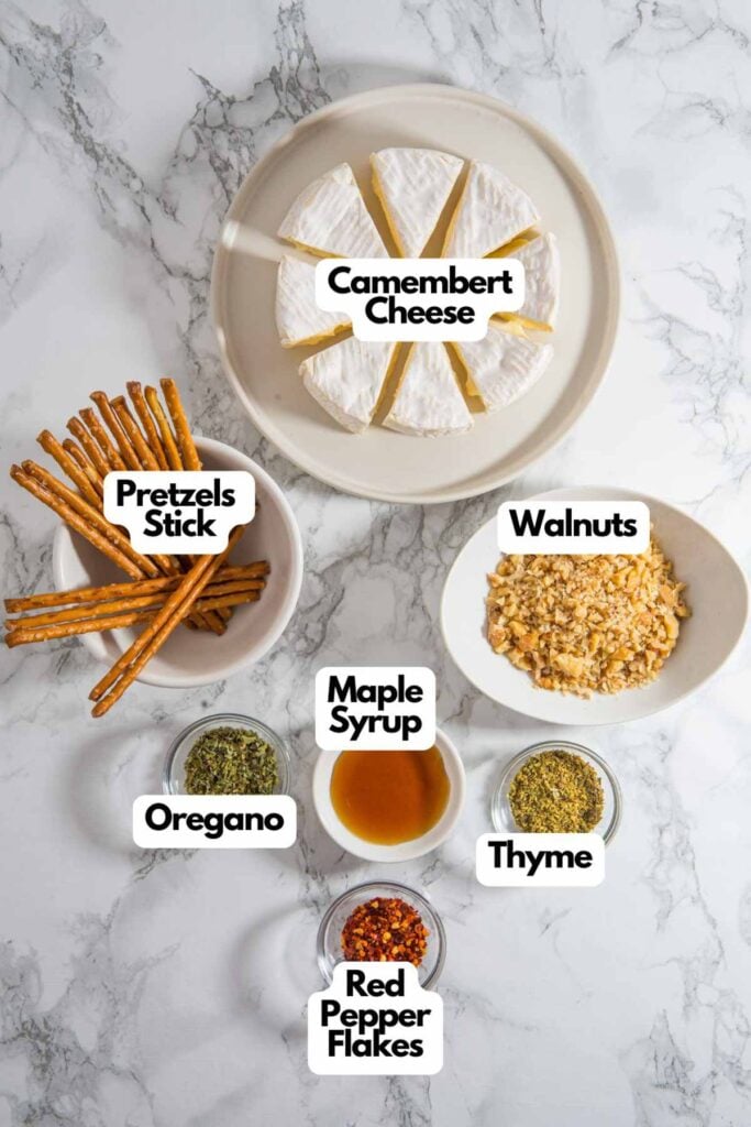 Ingredients for delightful Christmas cheese trees: Camembert slices on a plate, pretzel sticks as trunks, walnuts, and small bowls of maple syrup, oregano, thyme, and red pepper flakes elegantly arranged on a marble surface.