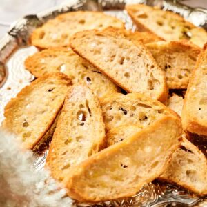A silver platter showcasing party crostini, with slices of toasted baguette elegantly surrounded by decorative greenery.