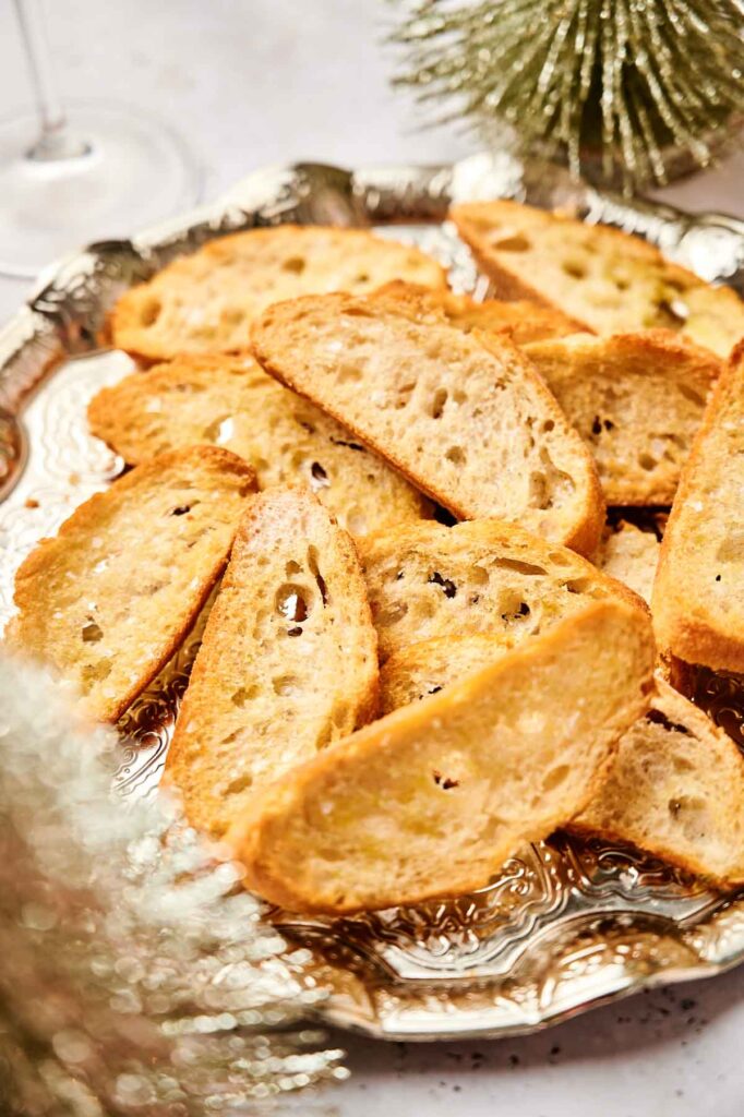 A silver platter showcasing party crostini, with slices of toasted baguette elegantly surrounded by decorative greenery.