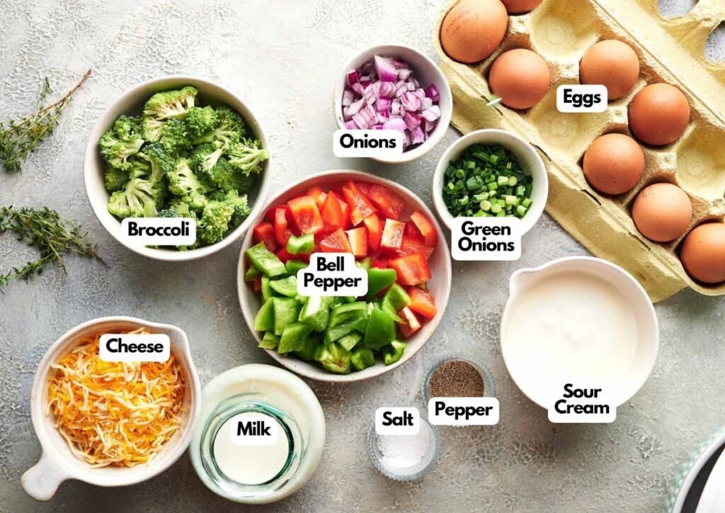 Top-down view of labeled ingredients for a chicken noodle casserole recipe, including eggs, broccoli, onions, green onions, bell pepper, cheese, milk, salt, pepper, and sour cream.