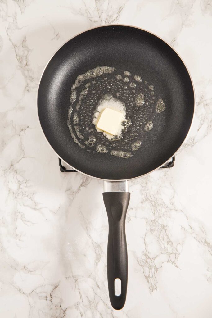 A non-stick frying pan with melting butter on a marble surface.