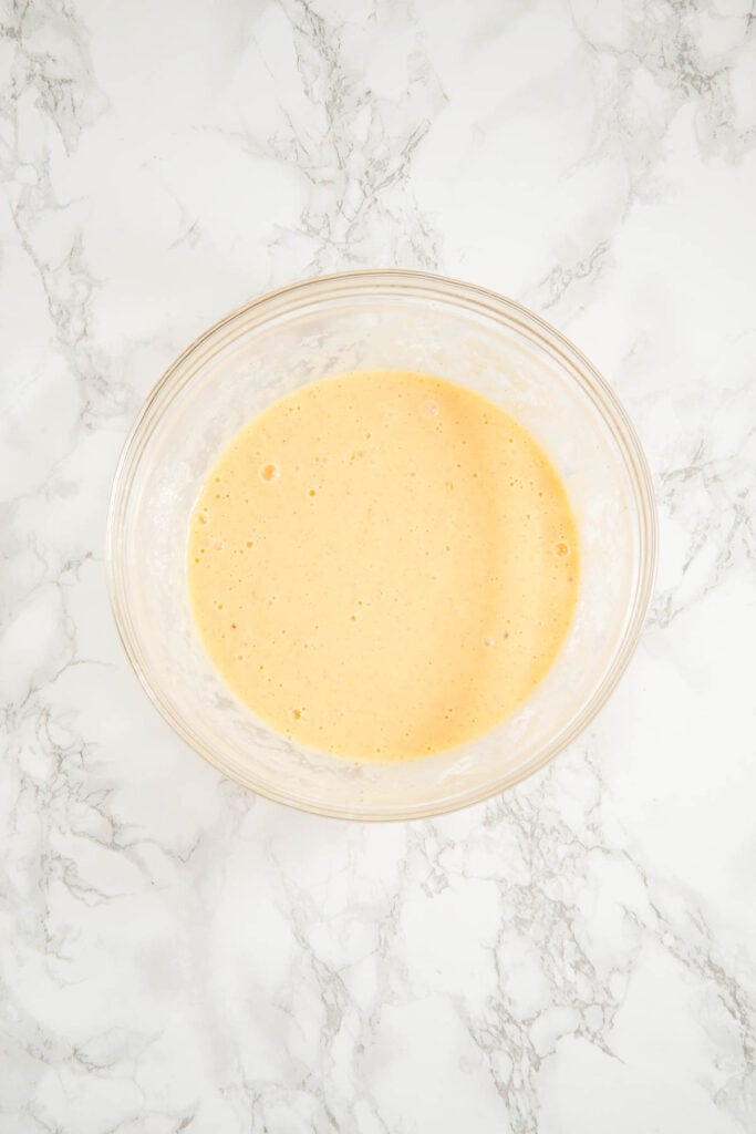 A clear glass bowl filled with a creamy, light yellow batter on a white marble surface.