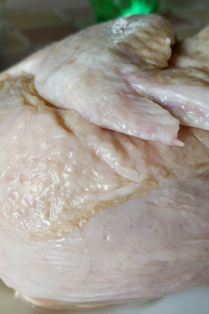 Close-up of raw chicken skin and meat on a white surface, with some textures and partial wings visible, resembling the initial stages of learning how to thaw a turkey.