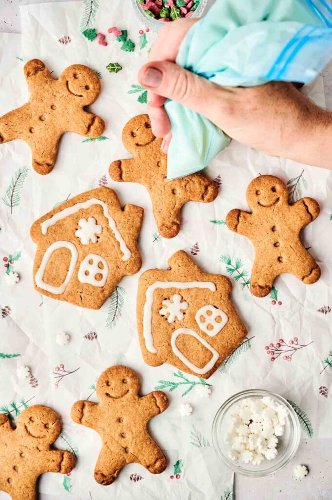 Hand icing gingerbread cookies shaped like people and houses on a festive table with decorative elements, featuring a batch of air fryer gingerbread cookies for a perfectly baked festive treat.