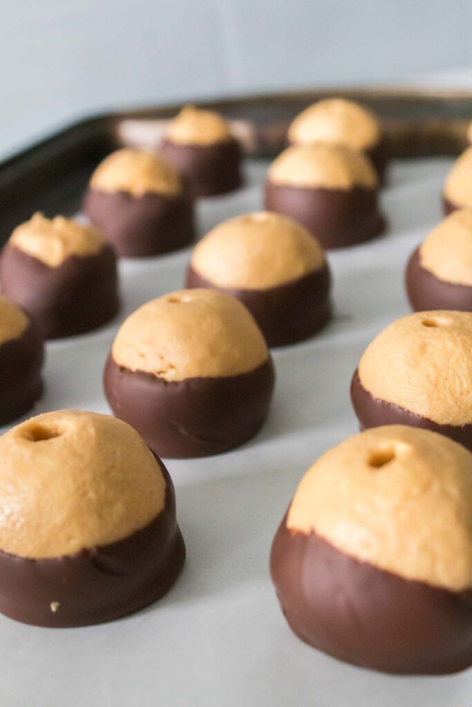 Several homemade buckeye candies, rich with peanut butter and coated in chocolate, are arranged on a baking sheet lined with parchment paper.