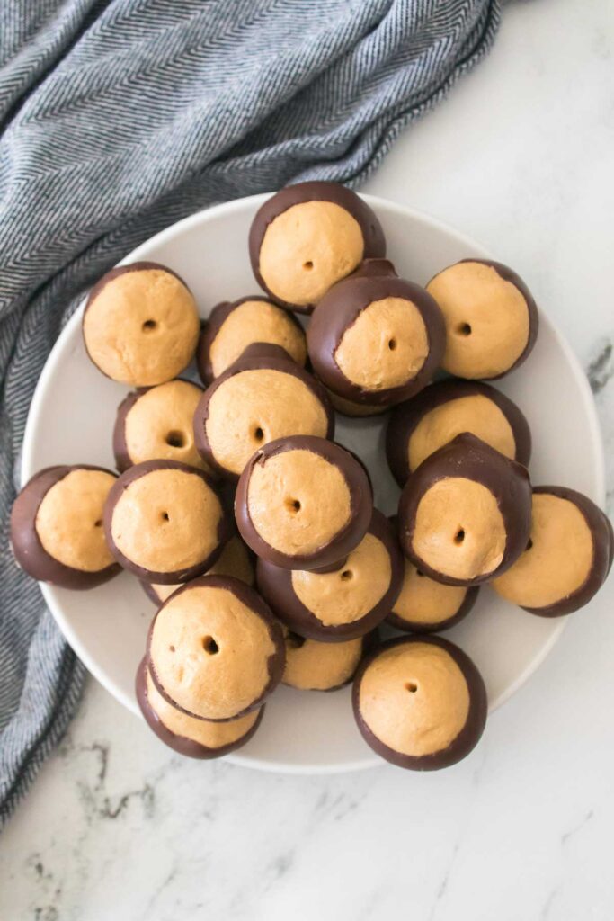 A plate of homemade buckeyes, those chocolate-dipped peanut butter balls, rests on a marble surface with a blue cloth nearby.