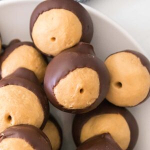 A plate of homemade buckeye candies, featuring round balls of peanut butter partially dipped in chocolate, with a textured cloth in the background.