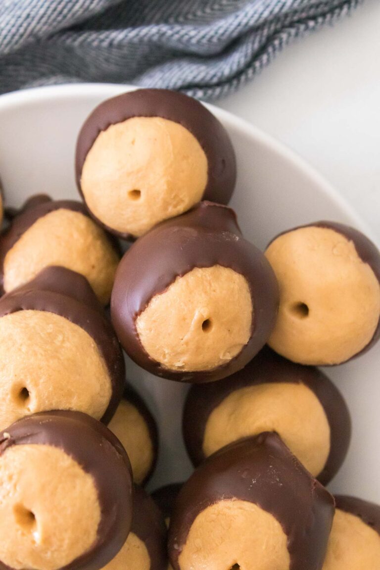 A plate of homemade buckeye candies, featuring round balls of peanut butter partially dipped in chocolate, with a textured cloth in the background.